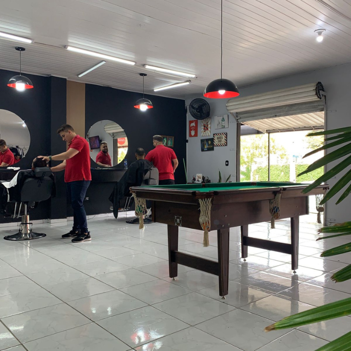Barbeiros atendendo clientes, com mesa de sinuca ao fundo, na Barbearia Império Ferreira